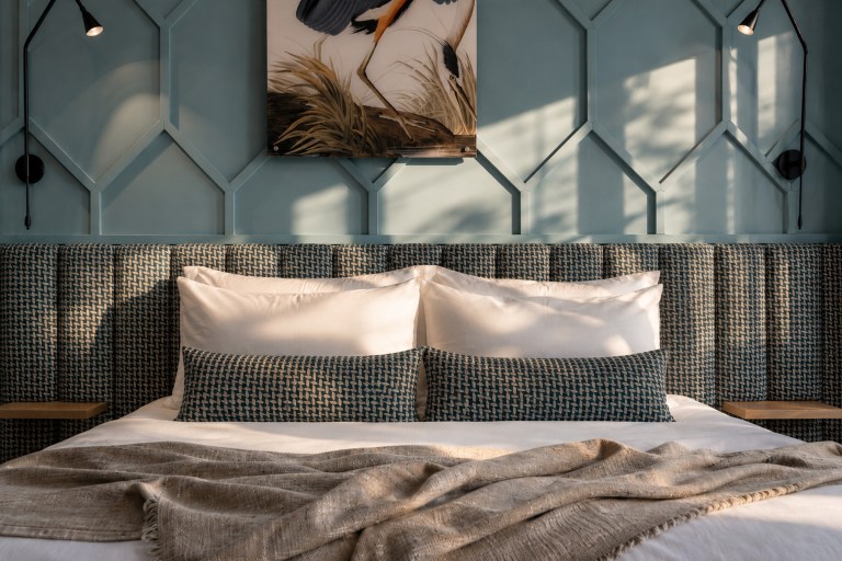 Hotel bedroom with a blue geometric feature wall, patterned headboard and layered cushions.