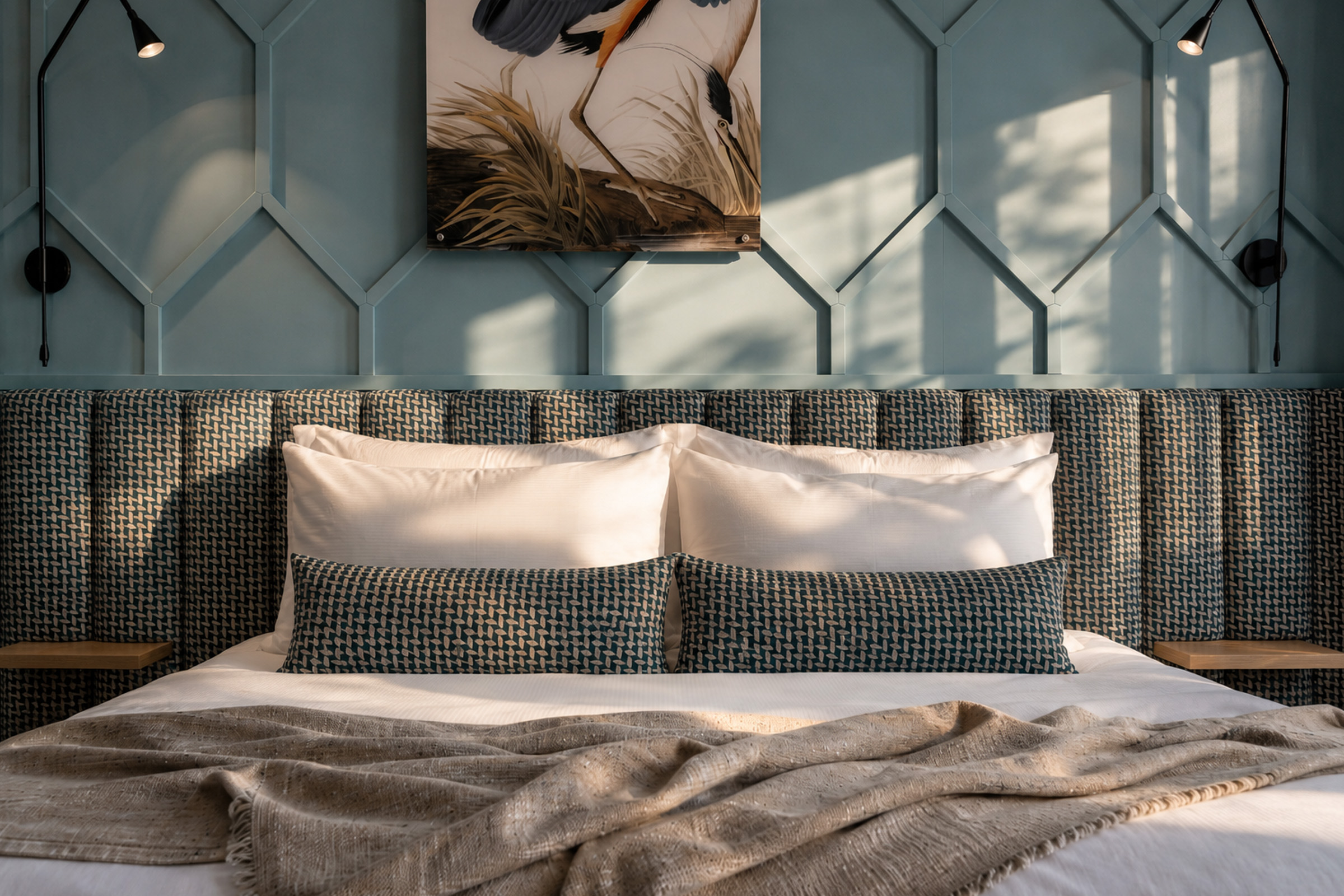 Hotel bedroom with a blue geometric feature wall, patterned headboard and layered cushions.